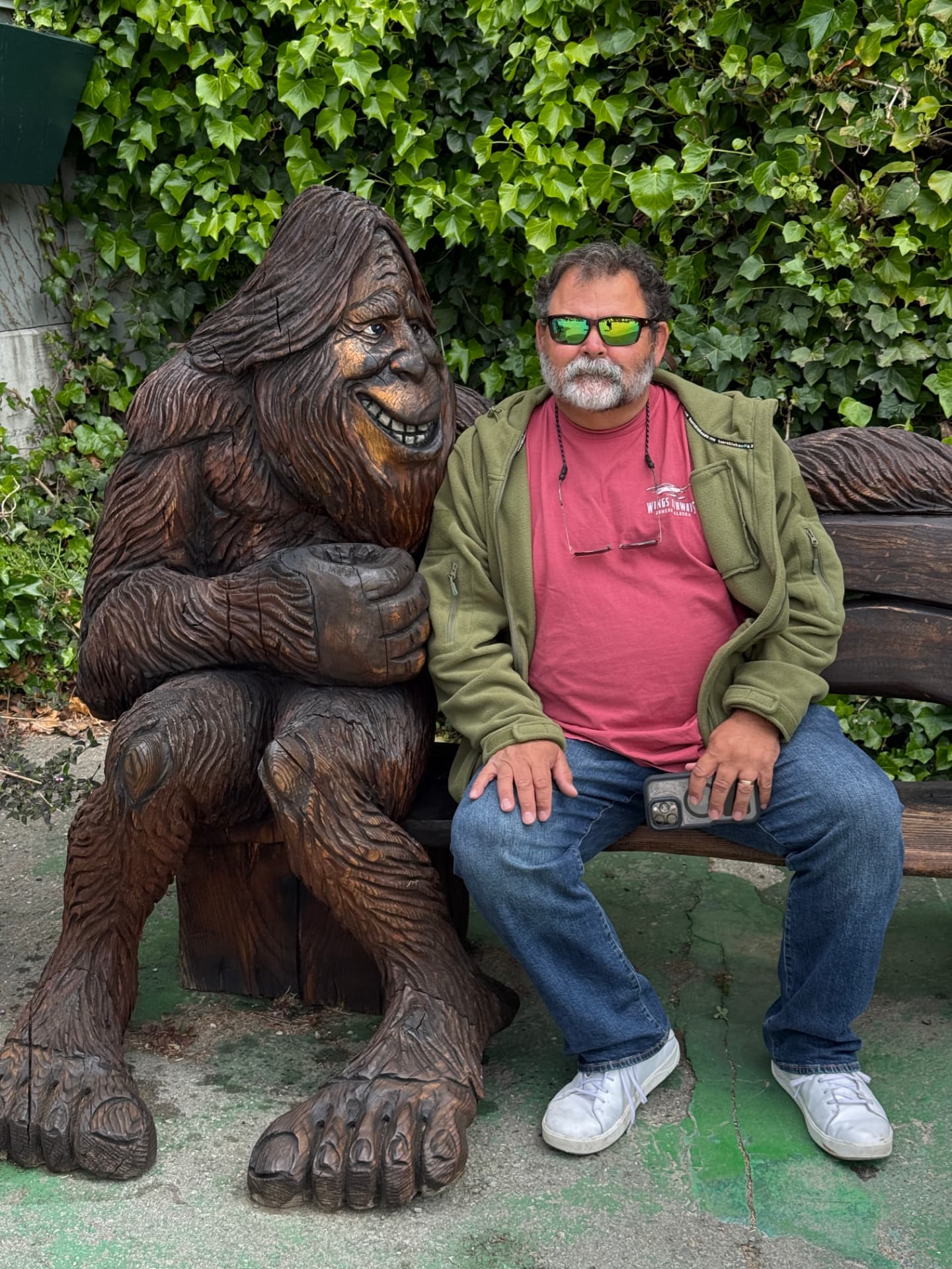 Evan Hightower seated beside a large carved wooden Bigfoot.